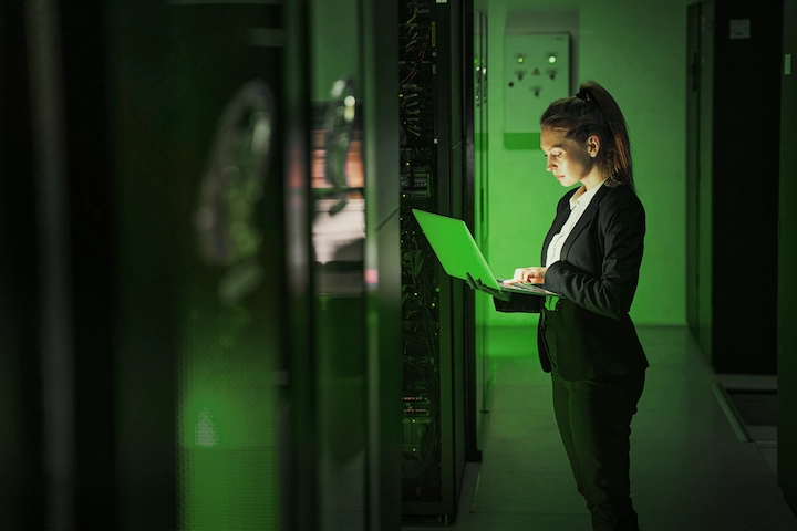 A person looking at a laptop in a server room